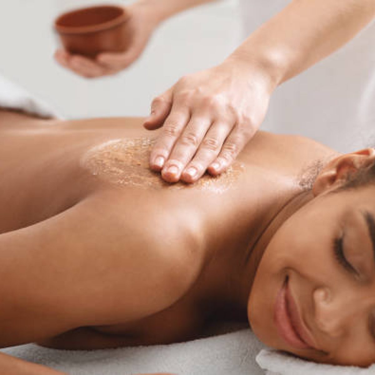 Beauty procedures at spa. Masseuse applying body scrub on black girl back, closeup